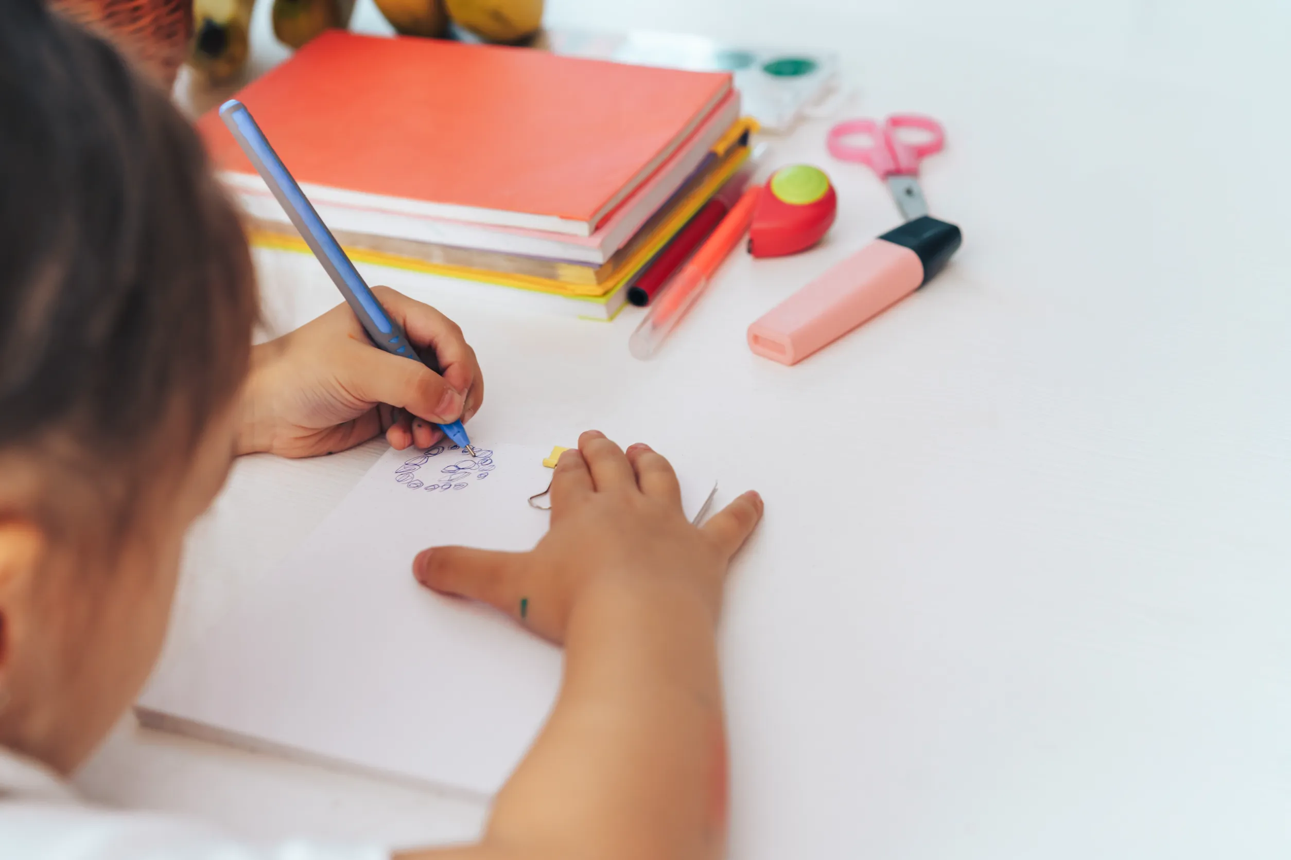 La jeune fille dessine avec un stylo bleu avec sa main gauche dans un cahier