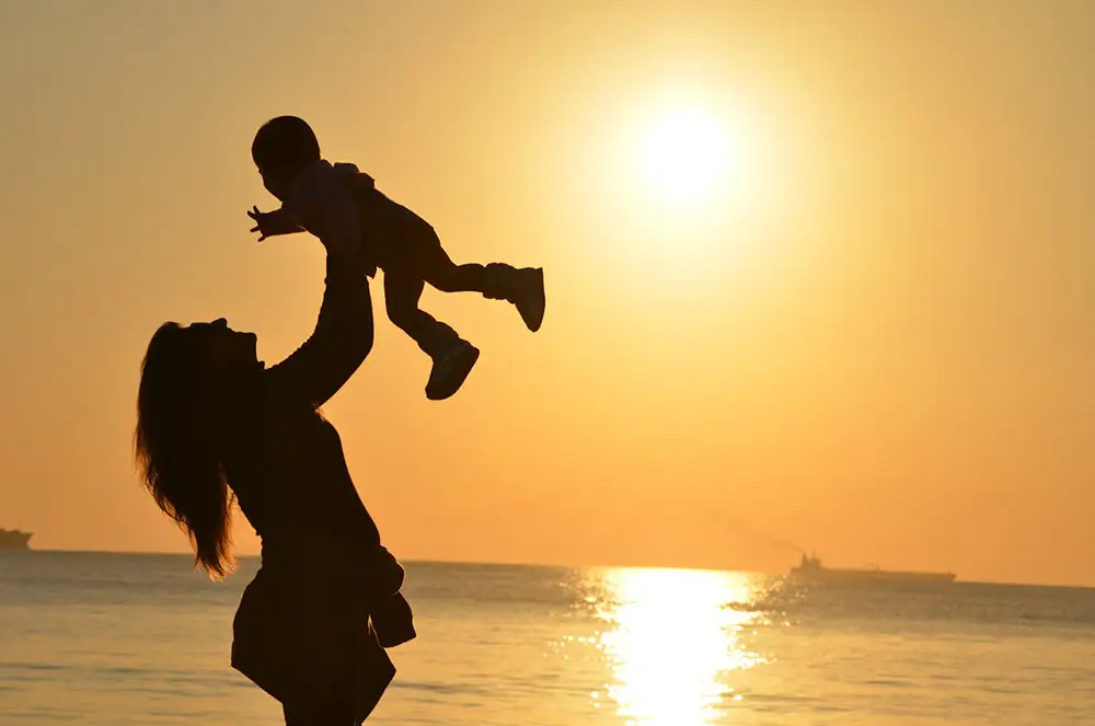 maman qui tient sa fille en hauteur sur une plage