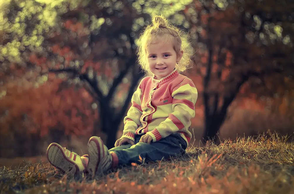 petite fille assise par terre sur une colline habillée pour l'automne avec une veste à boutons