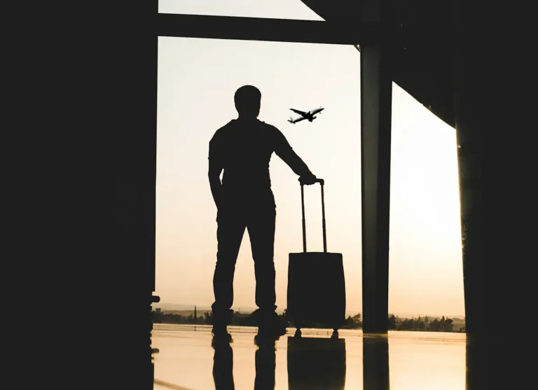 Homme avec sa valise dans un aéroport regardant un avion s'envoler par la fenêtre au coucher du soleil