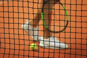 jambes d'une personne , balle de tennis, filet et raquette de tennis sur un court de terre battue
