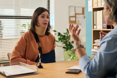 Indemnisation après un accident corporel: comprendre vos droits Personne avec bras en écharpe et minerve qui vient consulter une avocate pour une indemnisation après un accident de la route