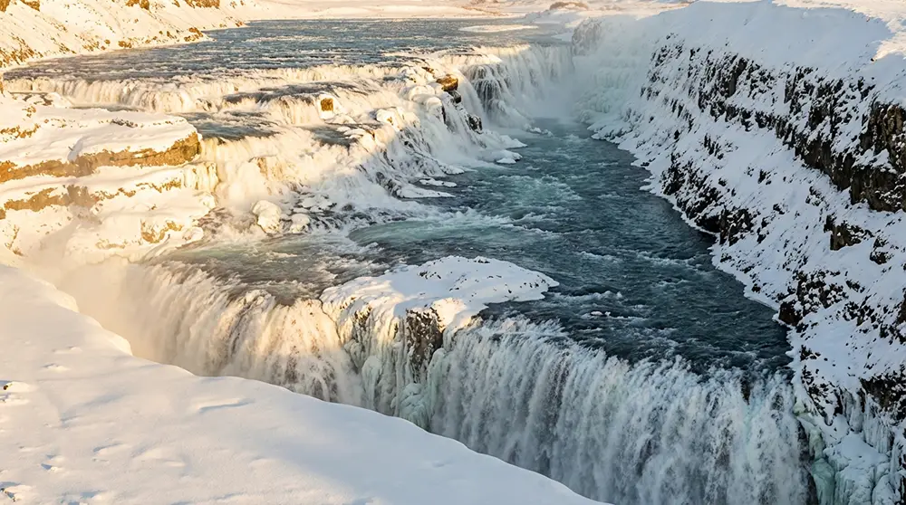 Cascade de Gullfoss en hiver avec glace et neige, canyon enneigé et lumière dorée rasante en Islande
