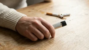E-cigarette et sevrage du tabac : les bonnes pratiques pour arrêter de fumer Personne tenant une e-cigarette moderne avec une cigarette cassée en arrière-plan symbolisant le sevrage du tabac