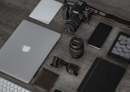Flat lay d'un espace de travail minimaliste avec appareil photo Canon, ordinateur portable MacBook, smartphone, lentilles et gadgets accessoires disposés sur table en bois gris