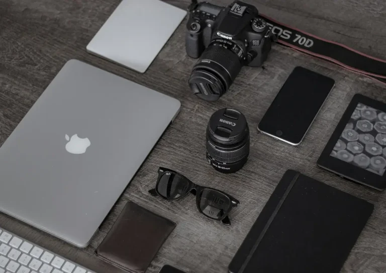 Flat lay d'un espace de travail minimaliste avec appareil photo Canon, ordinateur portable MacBook, smartphone, lentilles et gadgets accessoires disposés sur table en bois gris