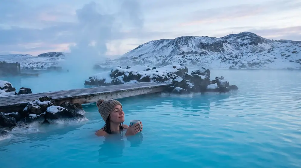 Personne se baignant dans des sources chaudes naturelles en Islande en hiver entourée de neige et montagnes