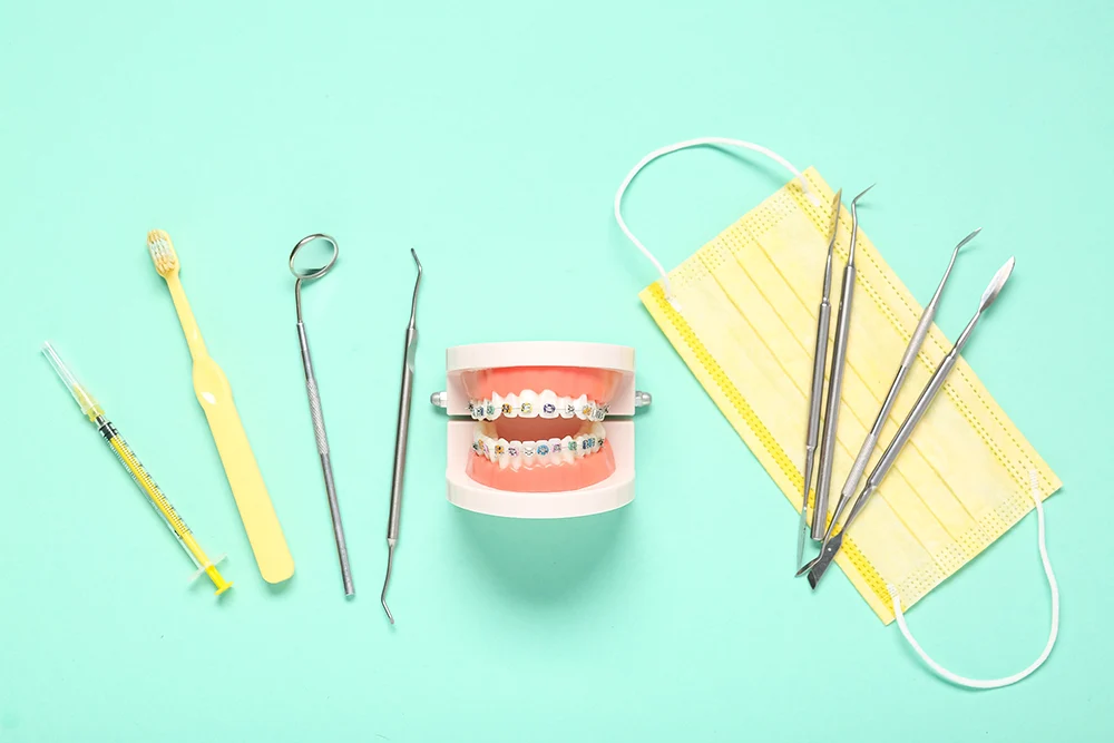 Instruments d'orthodontie, brossette, masque et modèle de mâchoire équipé de bagues sur fond vert menthe